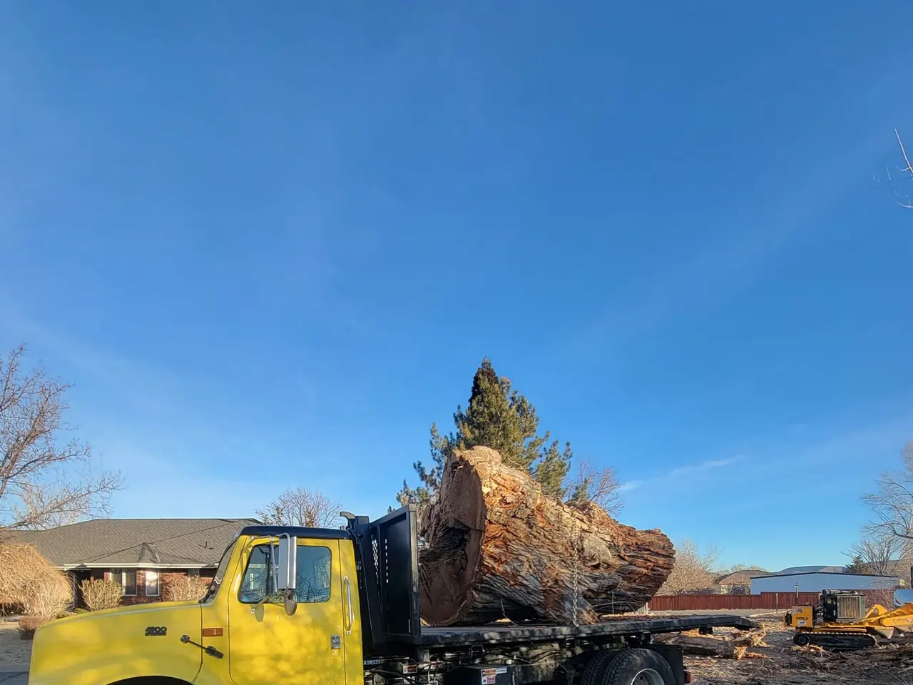 Yellow flatbed truck carrying one huge log round, blue sky